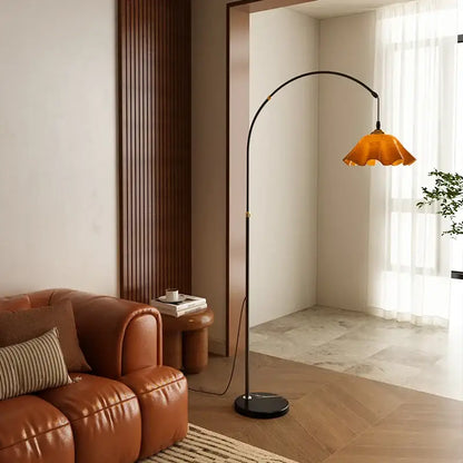 Curved black floor lamp with amber petal shade and living room shelf