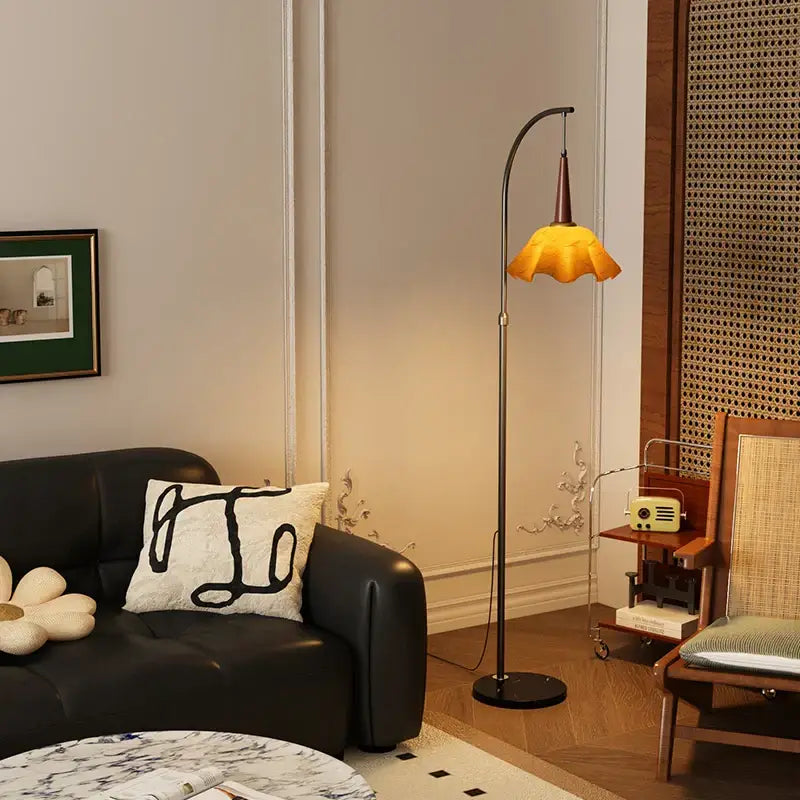 Curved black floor lamp with amber petal shade and living room shelf