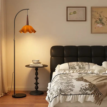 Curved black floor lamp with amber petal shade and living room shelf