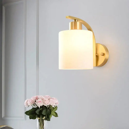 Modern brass cylinder wall sconce with milk glass shade bedroom light