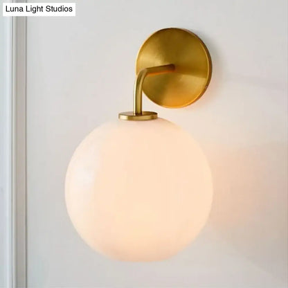 Modern brass wall lamp with clear white glass globe – bedroom