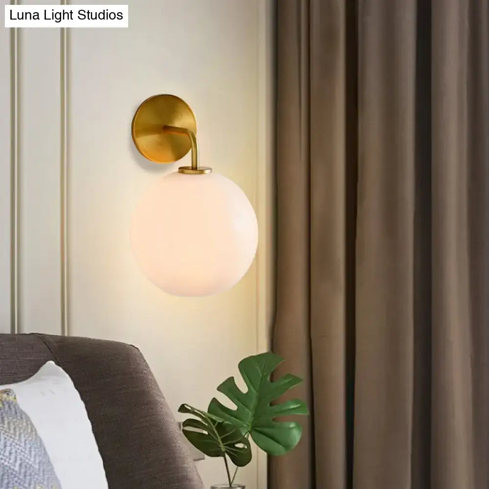Modern brass wall lamp with clear white glass globe – bedroom