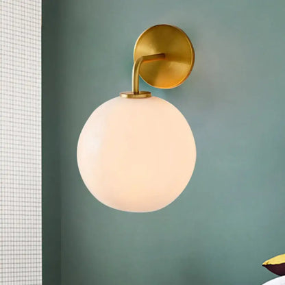 Modern brass wall lamp with clear white glass globe – bedroom