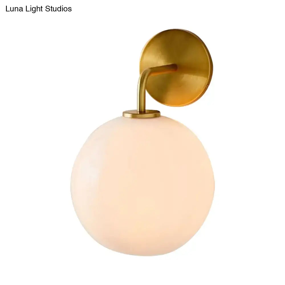Modern brass wall lamp with clear white glass globe – bedroom