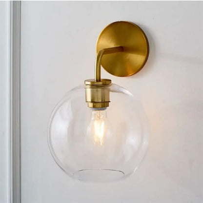 Modern brass wall lamp with clear white glass globe – bedroom