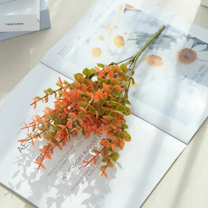 Orange & red artificial eucalyptus leaves in white pitcher – garden decor